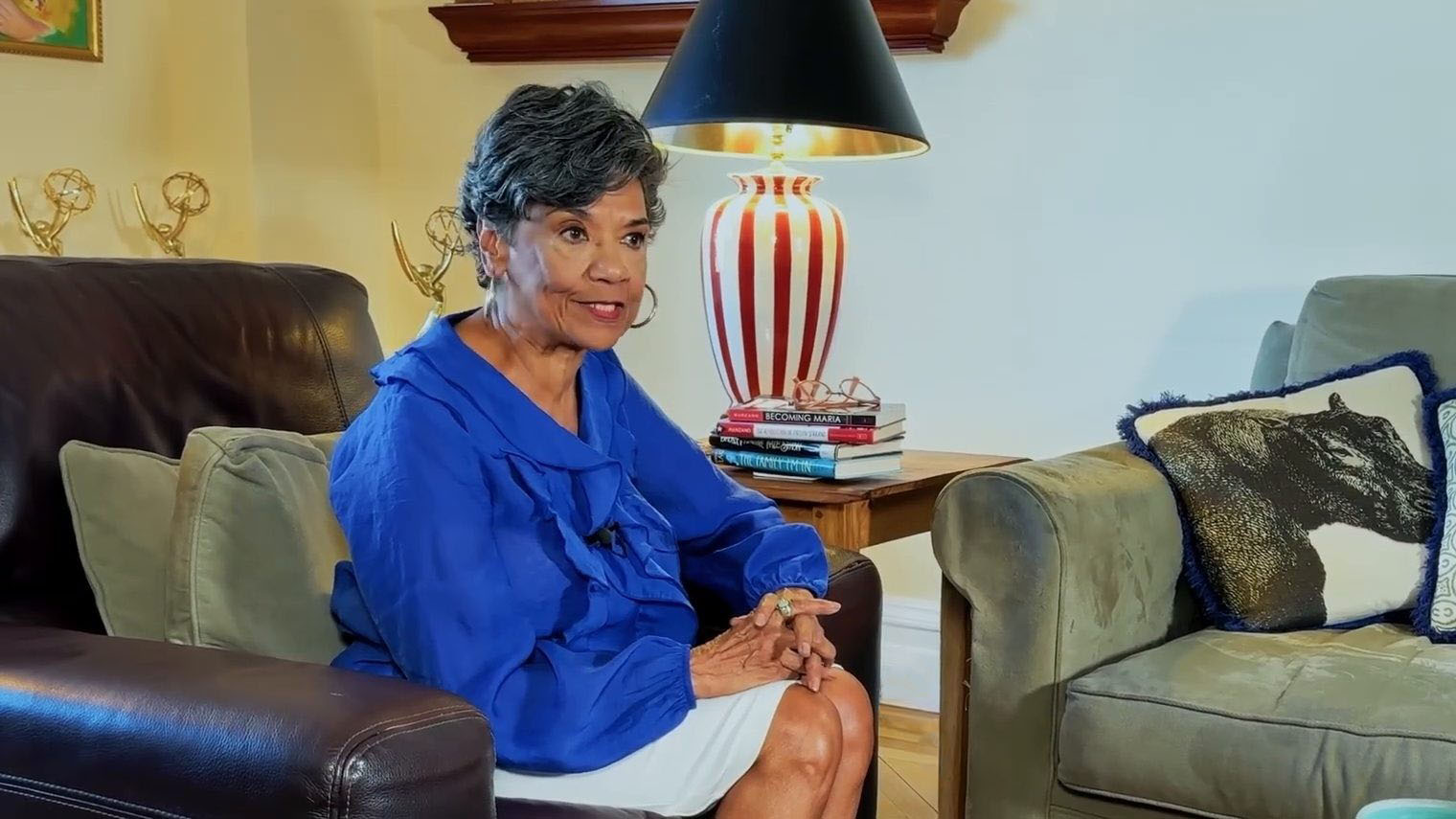 Sonia Manzano in a leather armchair at home, with her Emmy statuettes and a striped lamp behind her